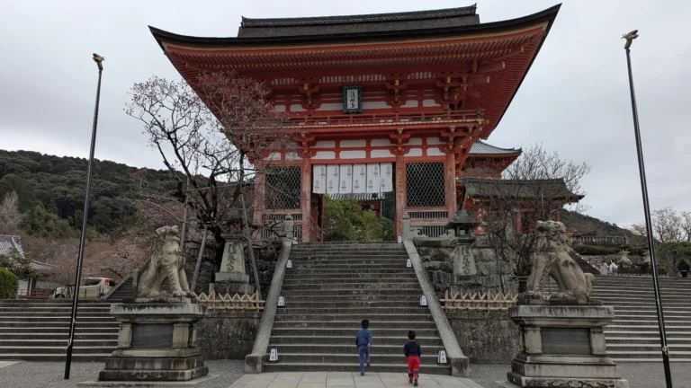 The vivid red Niomon Gate of Kiyomizu-dera Temple in Kyoto glows in the soft morning light as a family explores the peaceful approach path, part of a family-friendly Kyoto temple experience.