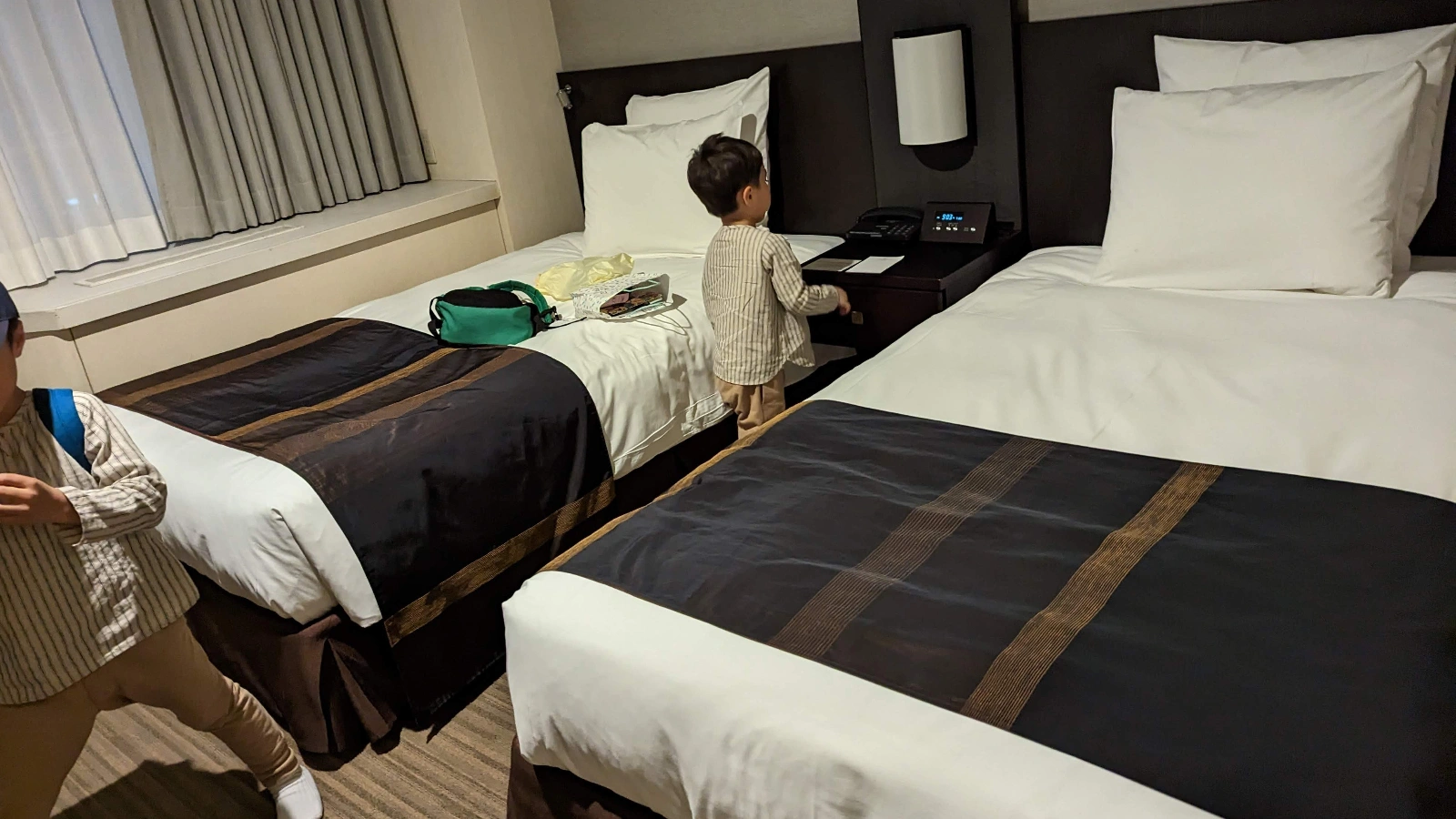 Twin-bed hotel room in Kobe with two young children exploring the space, a typical family-friendly stay near Harborland or Sannomiya.