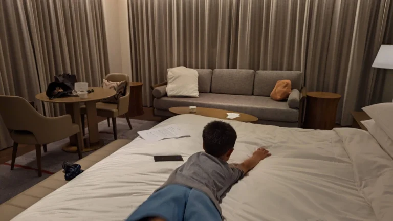 A modern family-friendly hotel room in Kyoto with Luca relaxing on the bed, ideal for travelers searching for the best hotels in Kyoto for families, featuring a cozy sofa, dining table, and soft lighting for a comfortable stay.