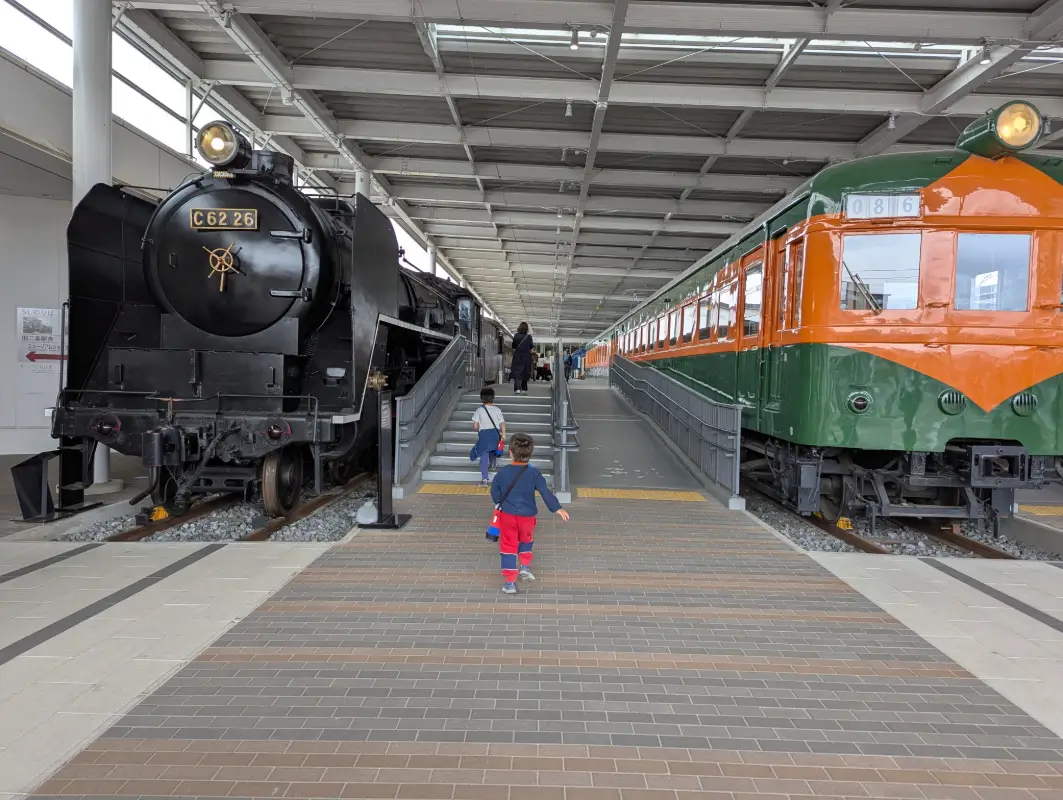 Luca & Nico walking between historic trains at the Kyoto Railway Museum, a hands-on experience perfect for families visiting Kyoto with kids.