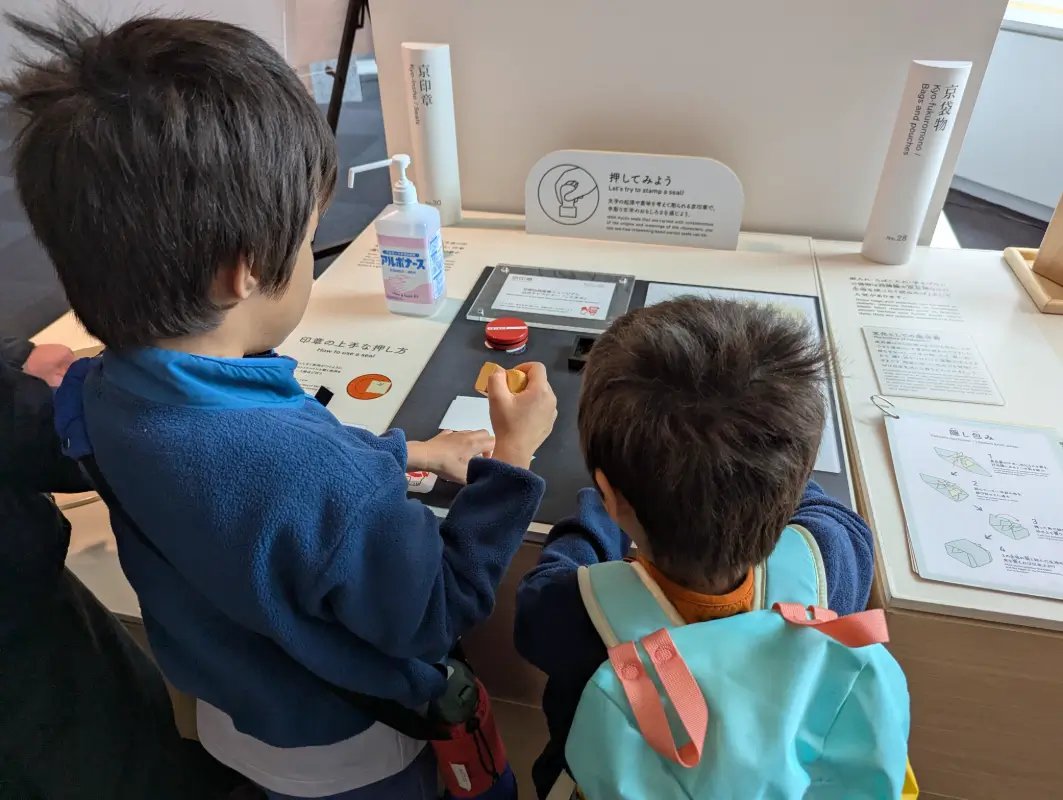 Luca & Nico trying a hands-on stamp activity at the Kyoto Traditional Crafts Museum, part of a family-friendly cultural experience