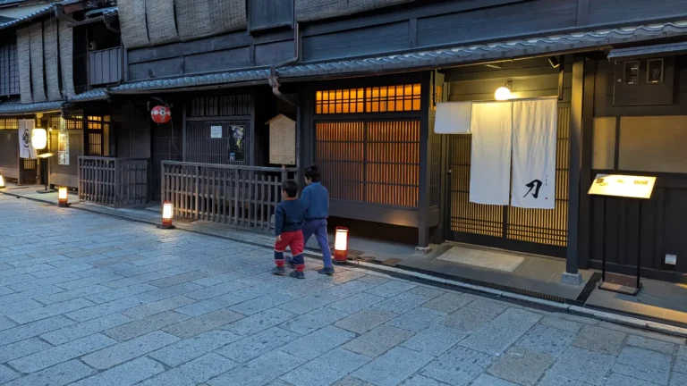 Luca & Nico walking along a lantern-lit traditional street in Kyoto’s Gion district at dusk, a peaceful cultural moment for families exploring Kyoto with kids.