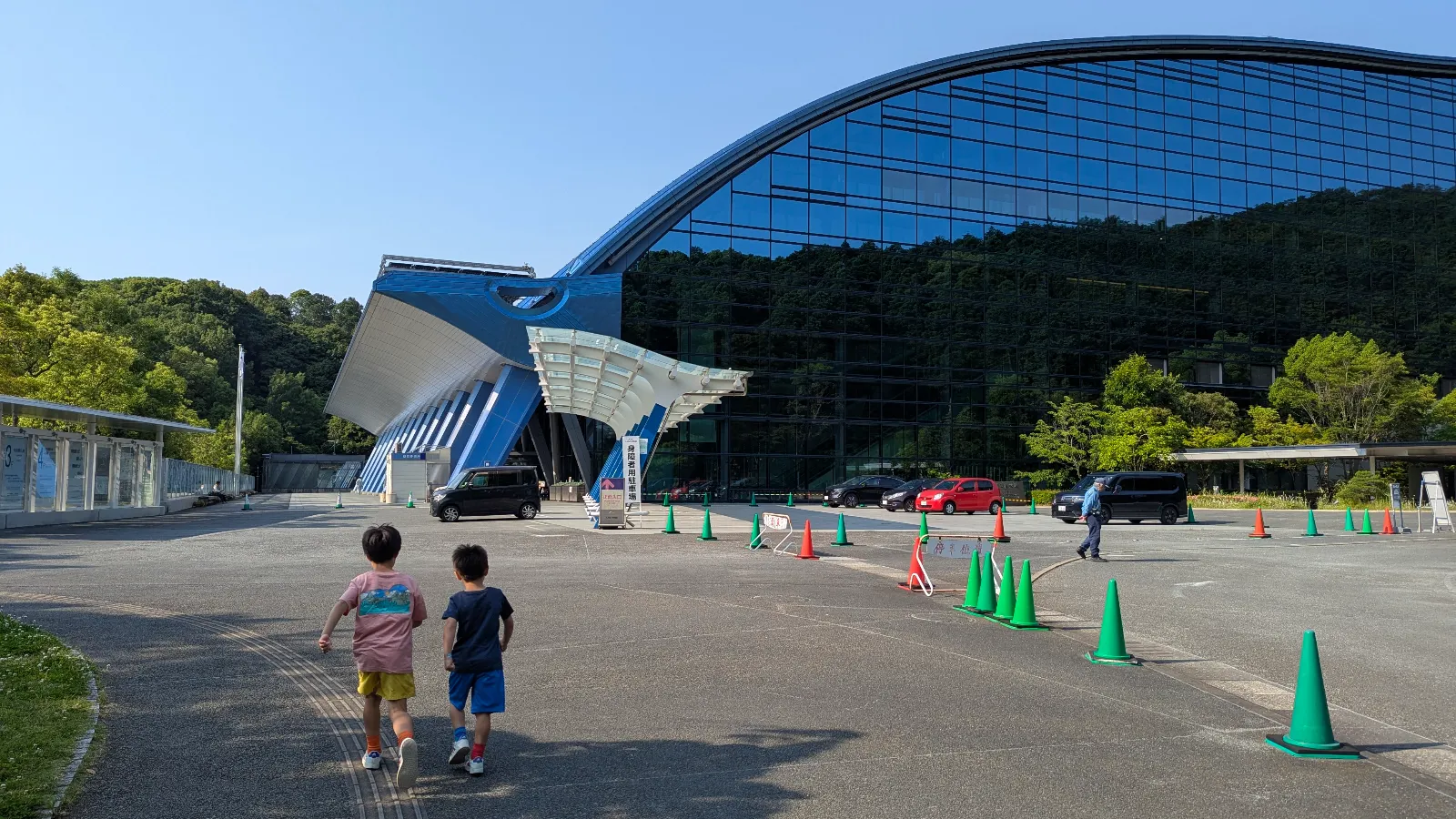 Luca and Nico walking toward the glass-fronted Kyushu National Museum in Dazaifu on a sunny day.