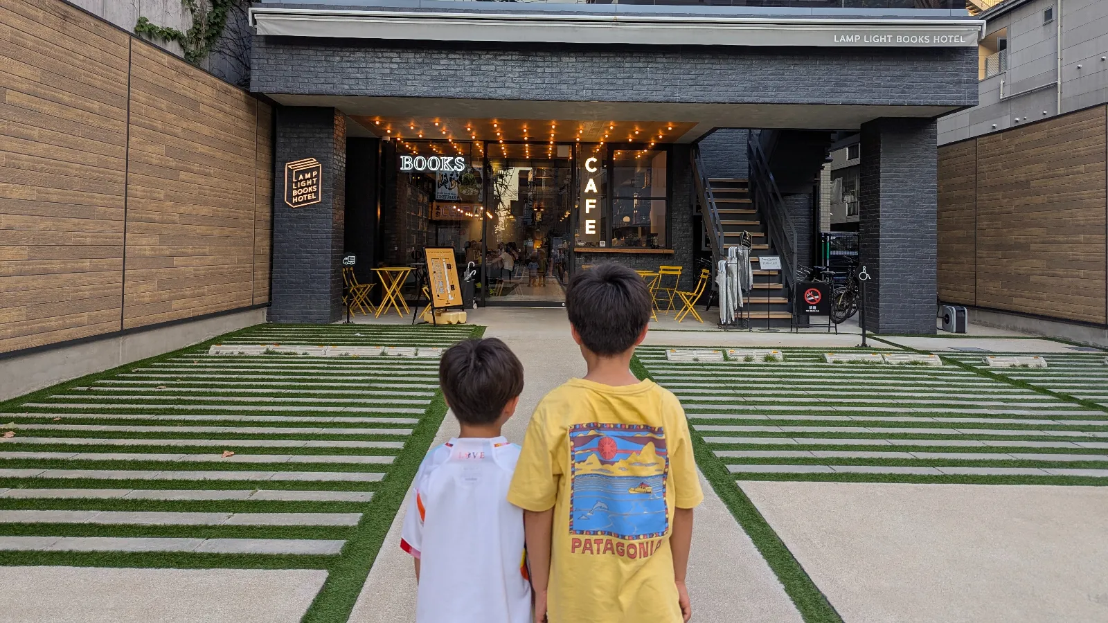 Luca and Nico walking toward the entrance of Lamp Light Books Hotel Fukuoka, a boutique family-friendly hotel with a 24-hour library café in Tenjin.