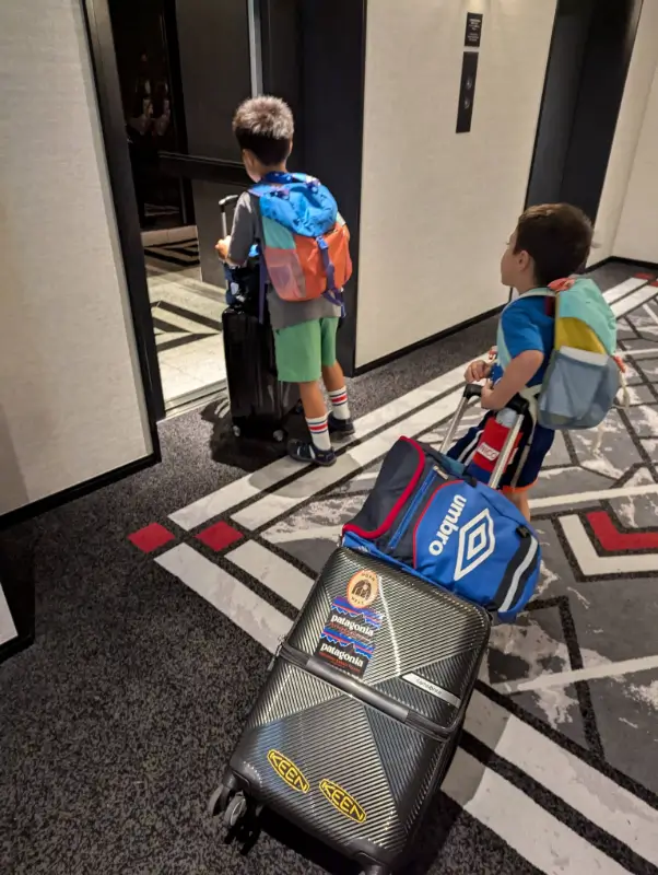 Luca & Nico independently pulling their suitcases into a hotel elevator in Japan, illustrating budget-conscious family travel with a focus on practical accommodations.