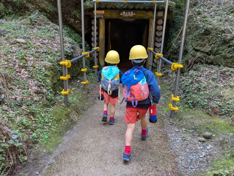 Luca & Nico wearing helmets and backpacks walking into the entrance of Iwami Ginzan silver mine in Japan, a spring family adventure with children