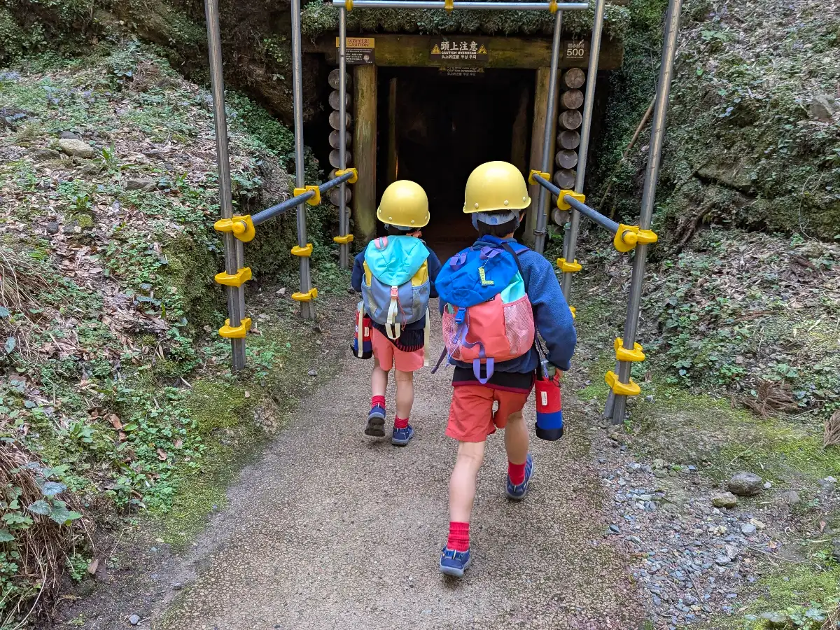Luca & Nico wearing helmets and backpacks walking into the entrance of Iwami Ginzan silver mine in Japan, a spring family adventure with children