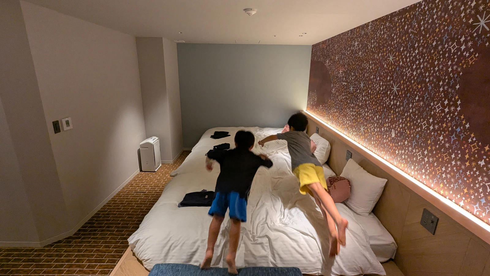 Two children jumping onto a large bed in a family-friendly hotel room in Japan.