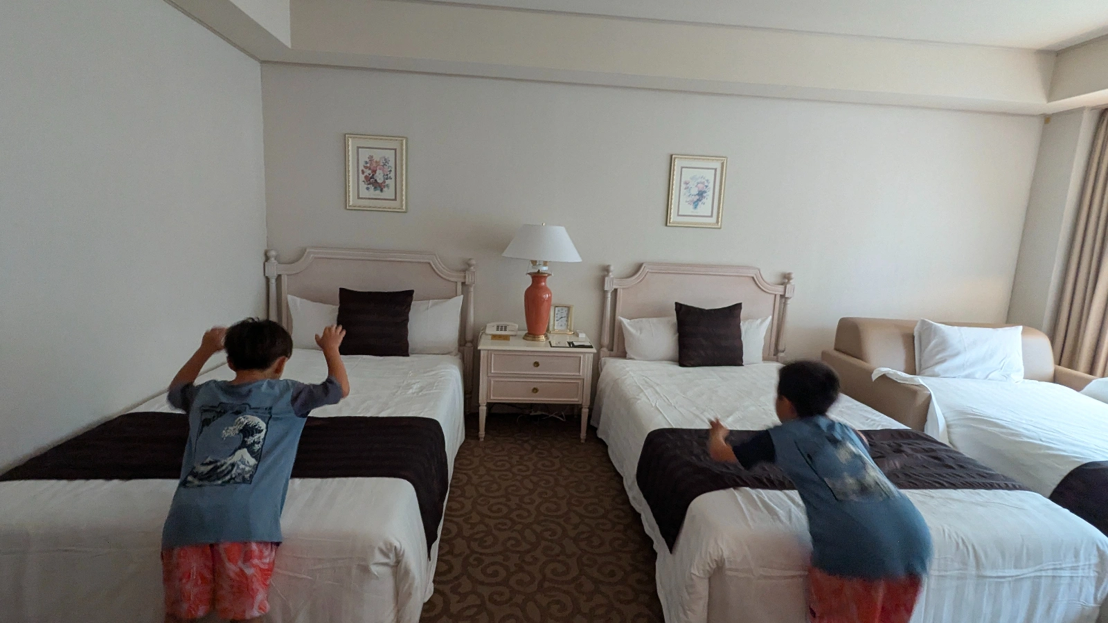 Two children playing on twin beds in a family-friendly hotel room in Japan.