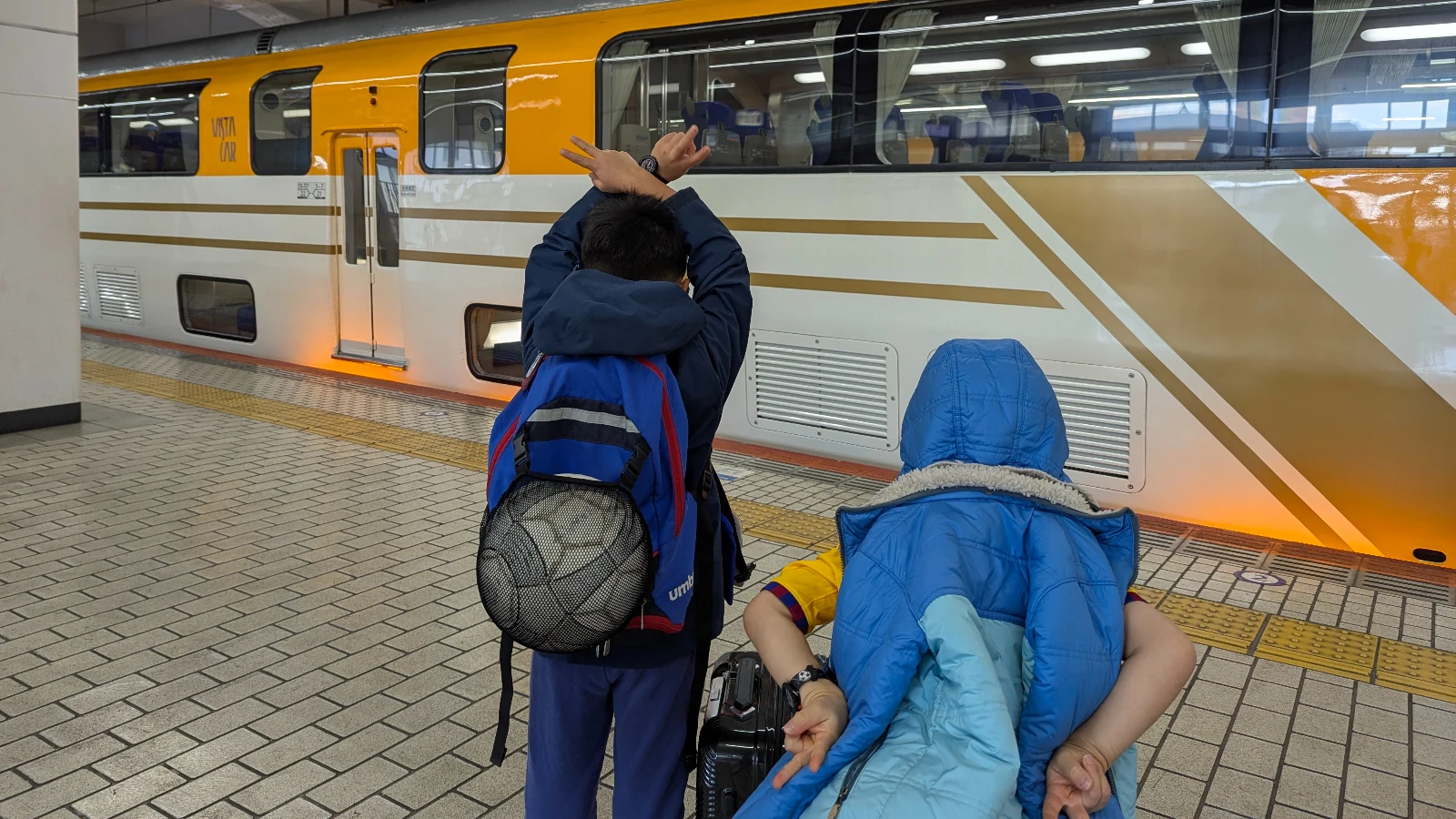 Luca and Nico in backpacks watching a Kintetsu Vista Car arrive at the platform in Osaka, Japan