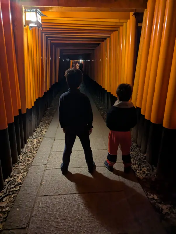 Luca & Nico exploring the illuminated torii gate tunnels at Fushimi Inari Shrine during a Kyoto itinerary with kids adventure
