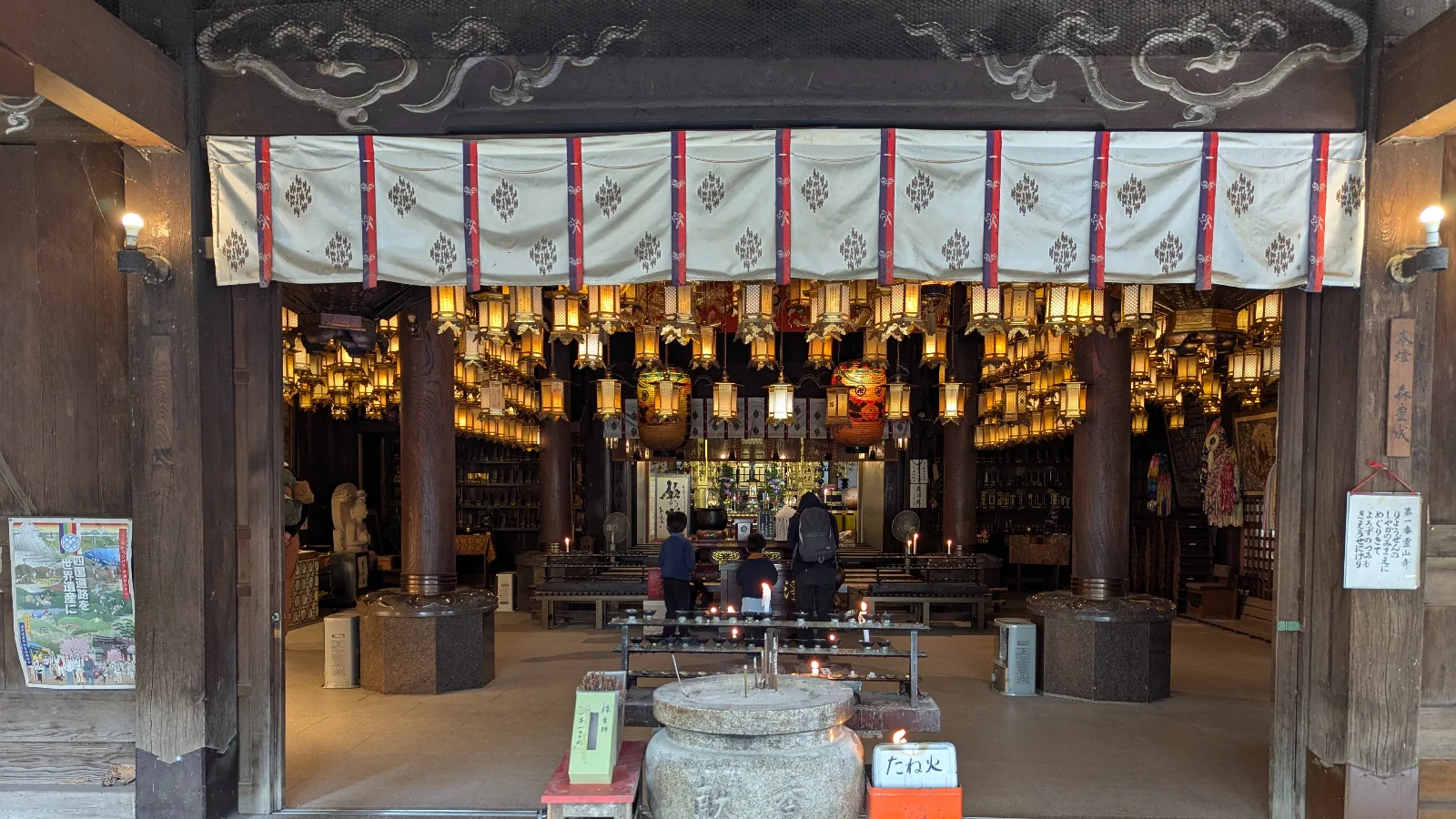 Luca and Nico praying among hanging lanterns at Ryozenji Temple main hall in Naruto, Tokushima.