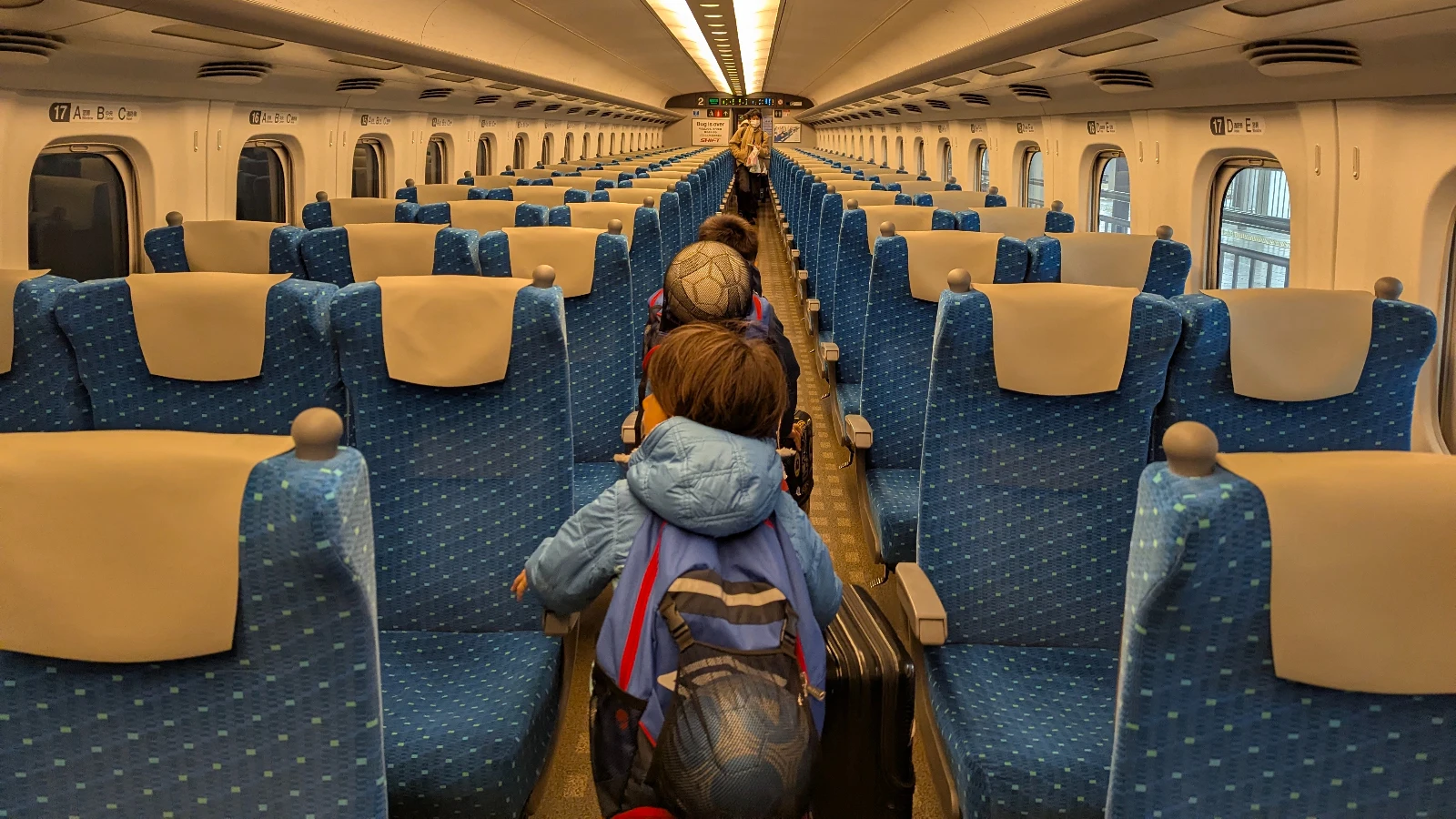 Two children walking down the aisle of an empty Shinkansen bullet train in Japan, pulling luggage during a family journey.