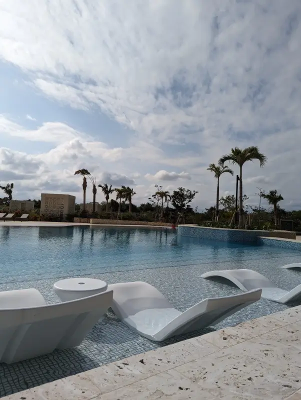 A serene resort pool with white loungers and palm trees under a cloudy sky in Miyakojima, Japan, representing the peaceful and luxurious side of family travel on the island.