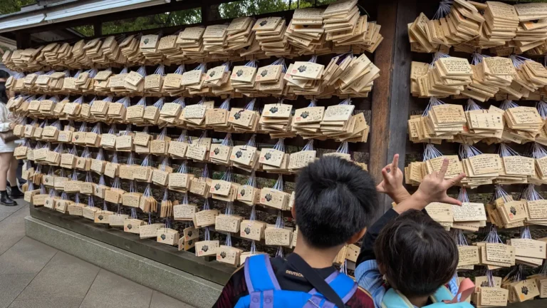 Two children looking at the ema wish plaques hanging at Meiji Jingu Shrine in Tokyo, surrounded by hundreds of handwritten wooden messages.