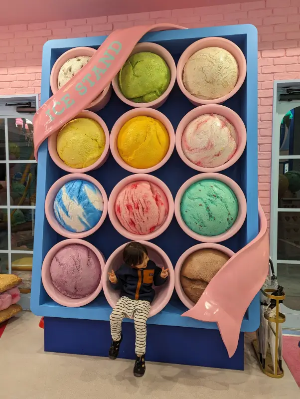 Nico sits inside a colorful photo booth shaped like giant ice cream scoops at a playful dessert shop in Miyakojima, highlighting fun and kid-friendly places to visit on the island.