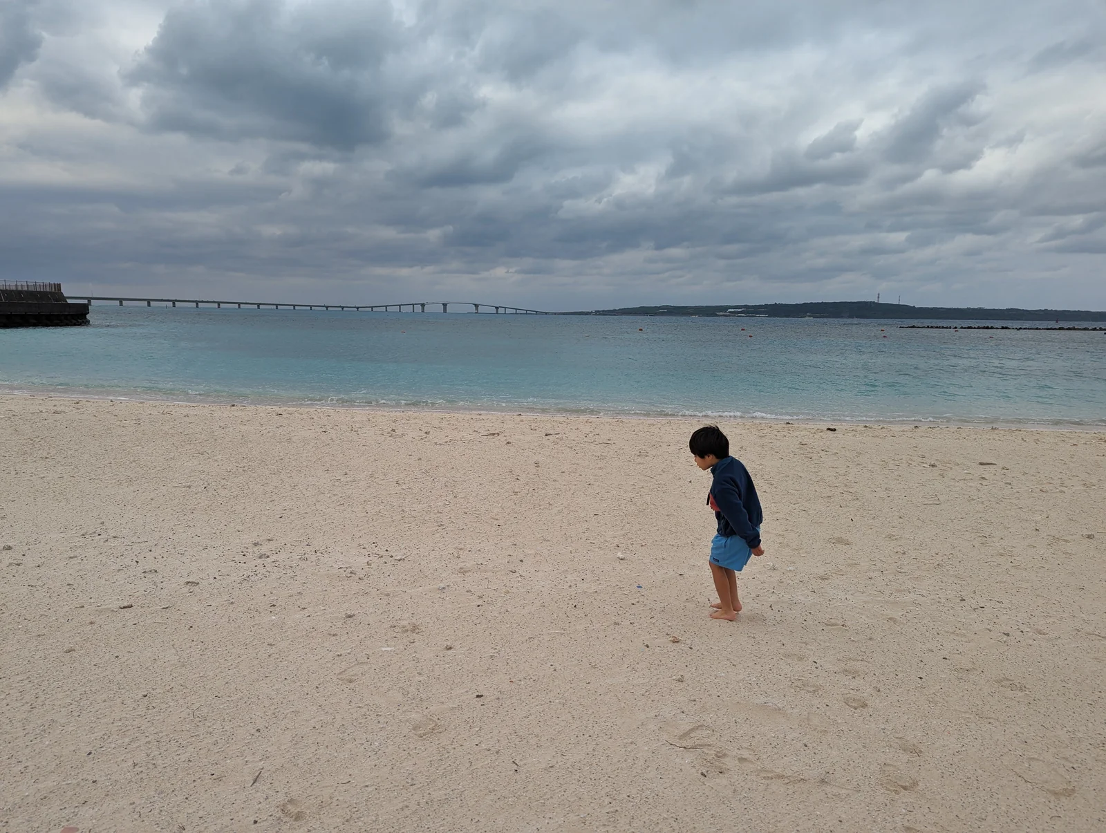A child on the white-sand beach with the long bridge on the horizon in Miyakojima, Okinawa Prefecture.