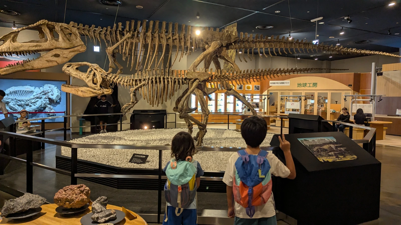 Luca and Nico stand at the rail below two large dinosaur skeletons at Fuji Nagoya Science Museum in Nagoya.