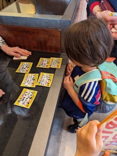 Nico with a pastel-colored Patagonia backpack carefully chooses a custom Tokyo DisneySea name tag while standing at a counter surrounded by vibrant character designs.