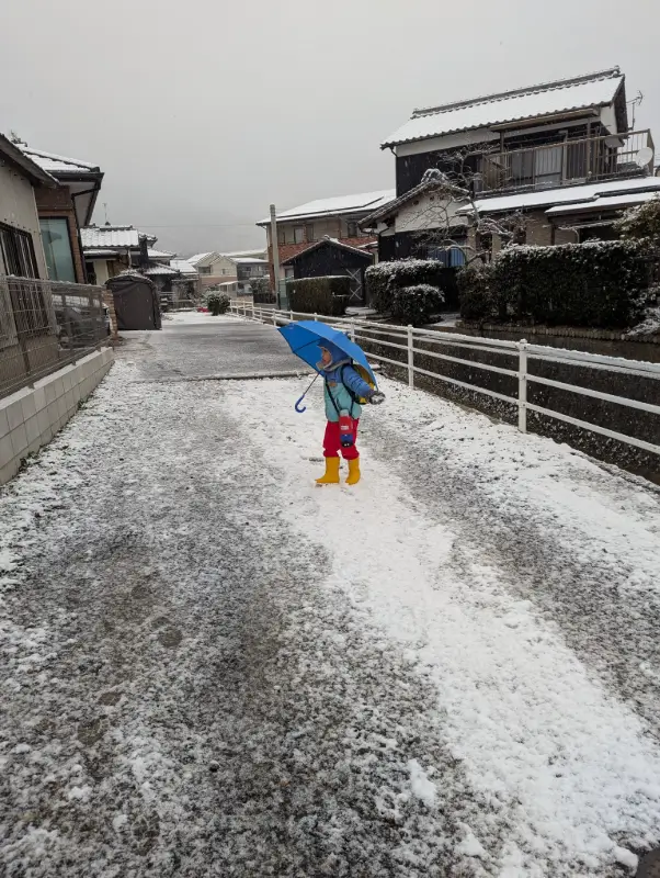 Nico walks through a snow-covered Japanese neighborhood holding a bright blue umbrella, capturing the peaceful charm of winter, one of the best times to visit Japan with kids for festive lights and quiet beauty.