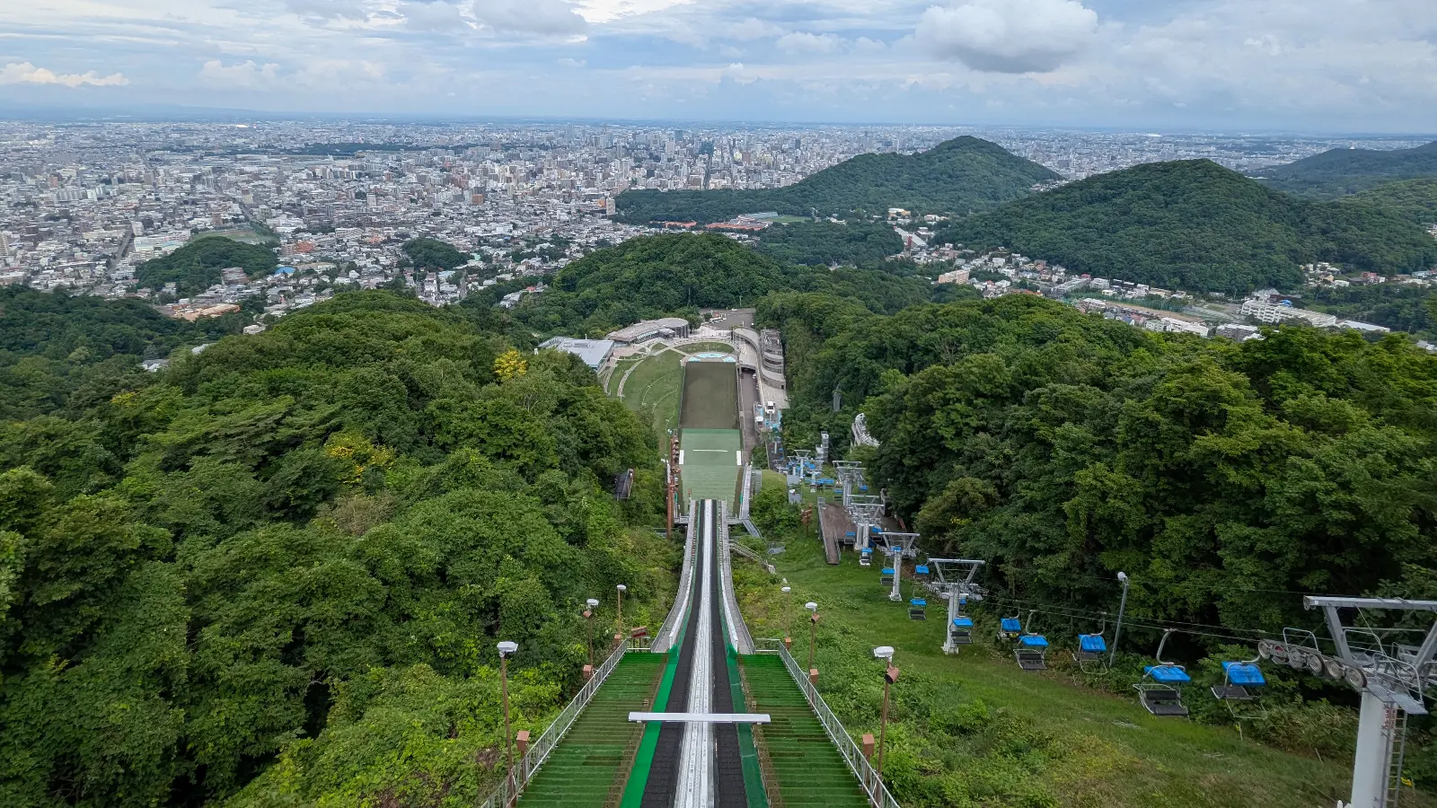 View from the Okurayama Ski Jump observation deck overlooking Sapporo city and green hills on a summer day.