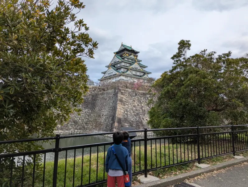 Luca and Nico looking up at the majestic Osaka Castle from behind the railing, capturing the excitement of family exploration in Japan.