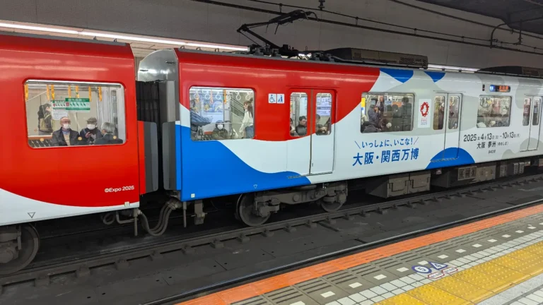 A red, white, and blue Osaka train decorated with Expo 2025 graphics at a subway platform, part of a spring family travel adventure in Japan.