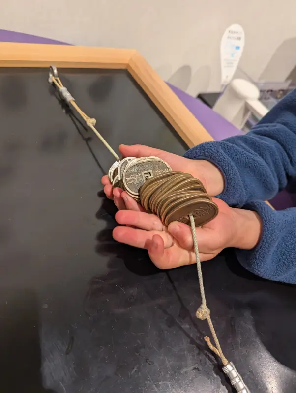 Close-up of Luca holding a string of replica Edo-era coins at the Osaka Mint Museum, part of a hands-on historical exhibit for kids.