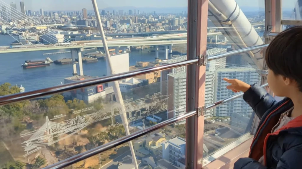 Luca pointing out Osaka Bay from inside the Tempozan Giant Ferris Wheel, a popular family-friendly attraction known for its skyline views and affordable ticket price.