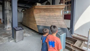 Two children look up at a vintage wooden train car at the Otaru Steam Locomotive Museum, exploring Japan’s early railway history on a family visit.