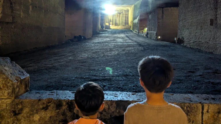 Two children standing inside Oya History Museum’s vast underground quarry in Utsunomiya, Japan, illuminated by soft light. A family exploring the historic stone mine where Japan’s history was carved from the earth.