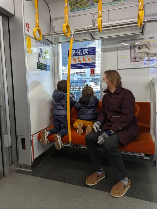 A father and two children dressed warmly, sitting in the priority seating area of a Japanese train, as the children look out the window, enjoying the ride.