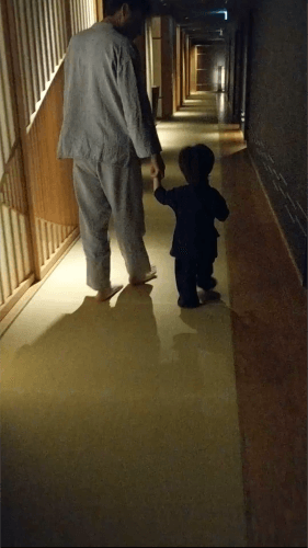 A father and child walk hand-in-hand down a softly lit, minimalist hallway with tatami flooring in a traditional Japanese ryokan, Hoshinoya Tokyo.