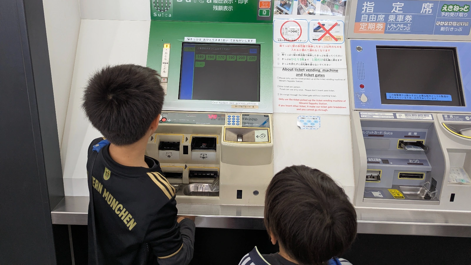 Two children using a Japanese train ticket machine at The Railway Museum, learning how to buy tickets during a family visit.