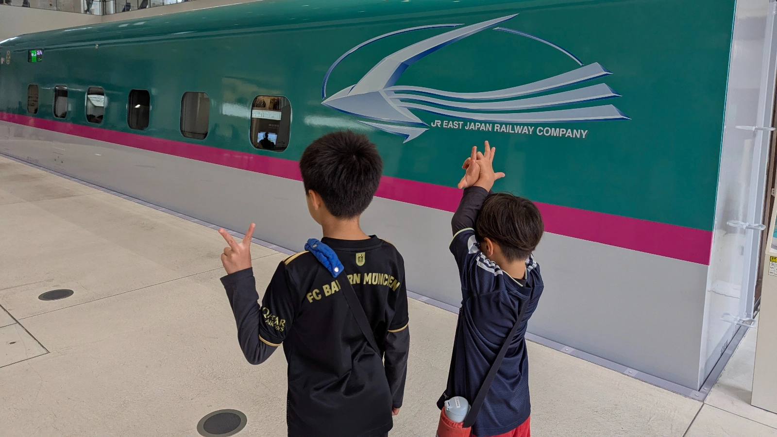 Two children standing in front of a full-size Shinkansen exhibit at The Railway Museum in Tokyo, excitedly posing during their visit.