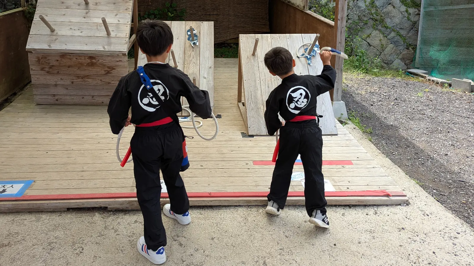 Two kids dressed as ninjas practice throwing stars at Saga Ninja Village, a fun hands-on family attraction in Saga, Japan.