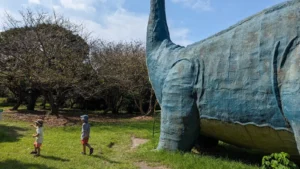 Luca & Nico walking beside a giant dinosaur statue at Sakurajima Dinosaur Park, one of the most unique free attractions in Kagoshima with kids.