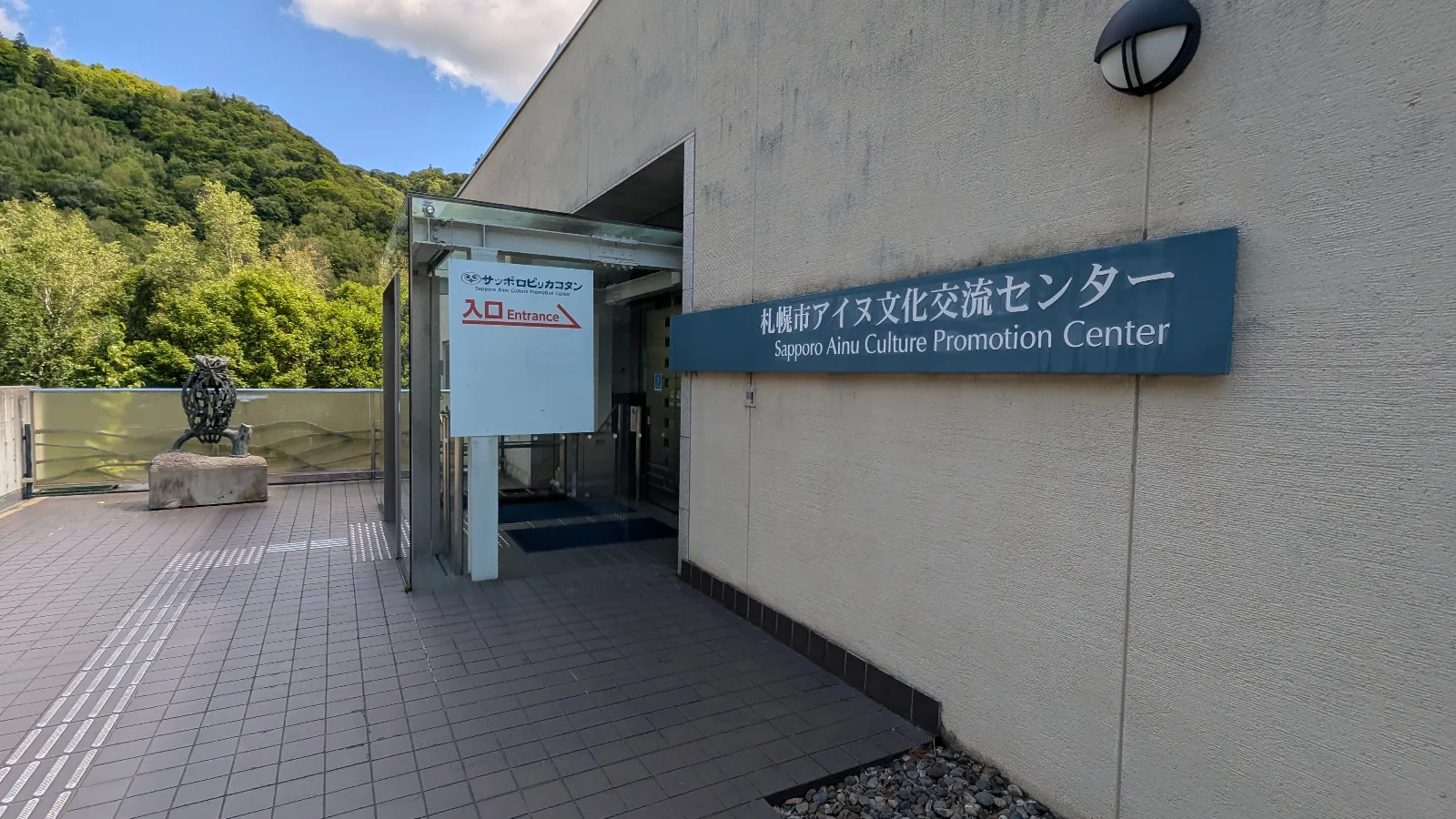 Entrance to the Sapporo Ainu Culture Promotion Center in Hokkaido, surrounded by green forest hills under a blue sky — family travel attraction in Sapporo.