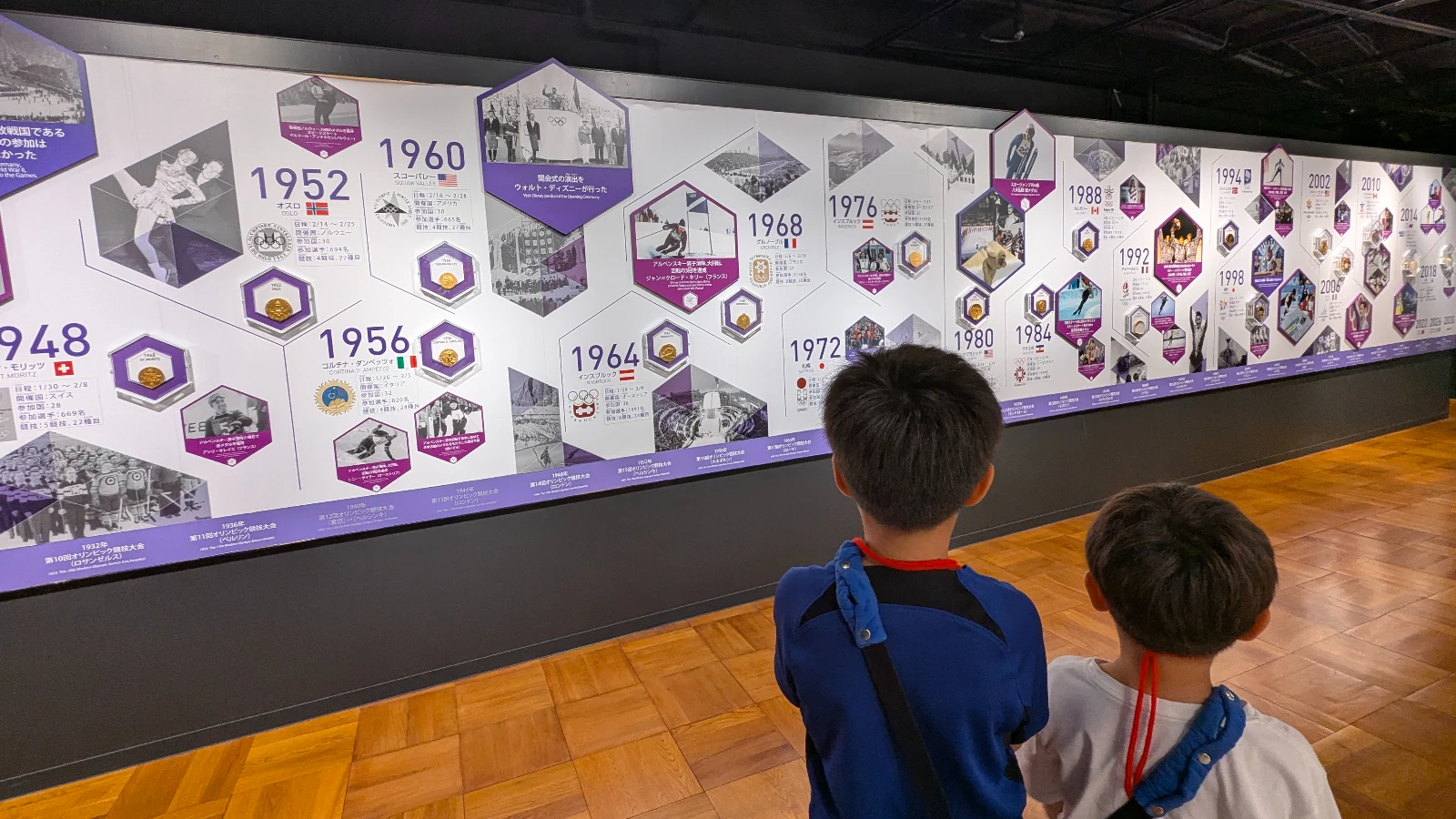 Children viewing the Olympic history timeline exhibit inside the Sapporo Olympic Museum, featuring highlights from the 1972 Winter Olympics.