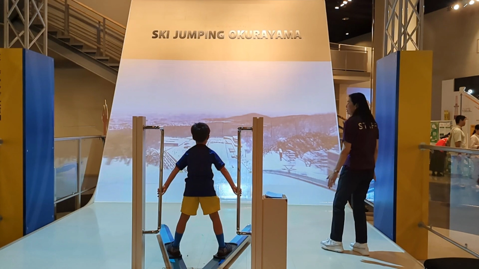 A child trying the ski jumping simulator at the Sapporo Olympic Museum inside the Okurayama Ski Jump Stadium, Japan family travel activity.