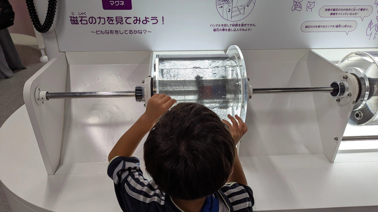 A child explores the magnetic force exhibit at Sapporo Science Center, turning handles to see how magnets interact through water and metal.