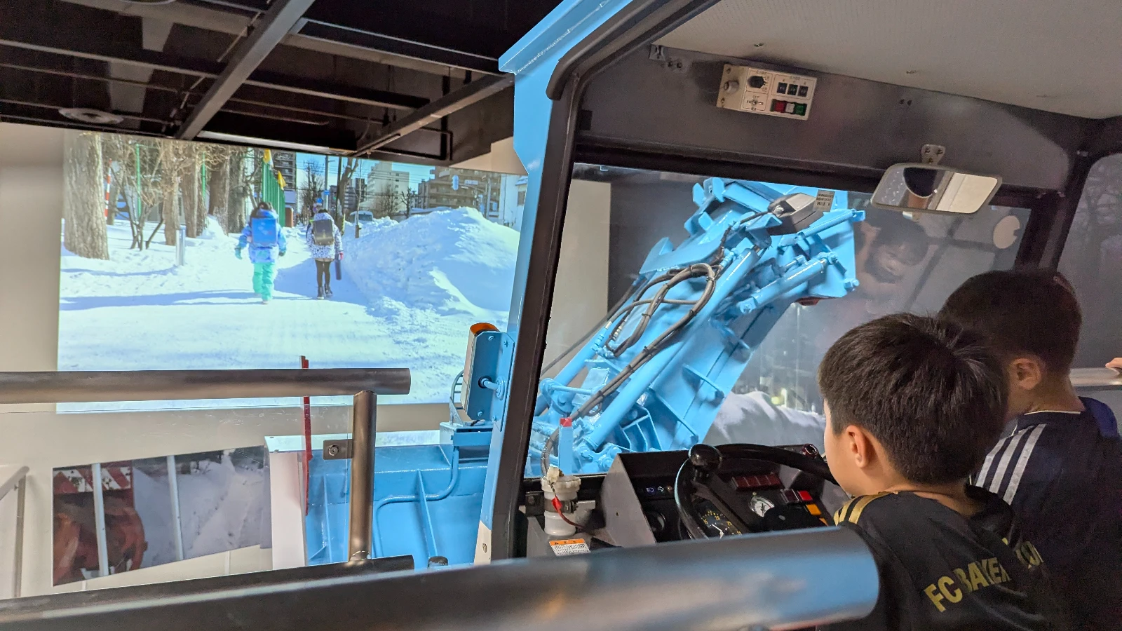 Two children explore the snowplow simulator exhibit at Sapporo Science Center, learning how Hokkaido clears winter streets through interactive displays.