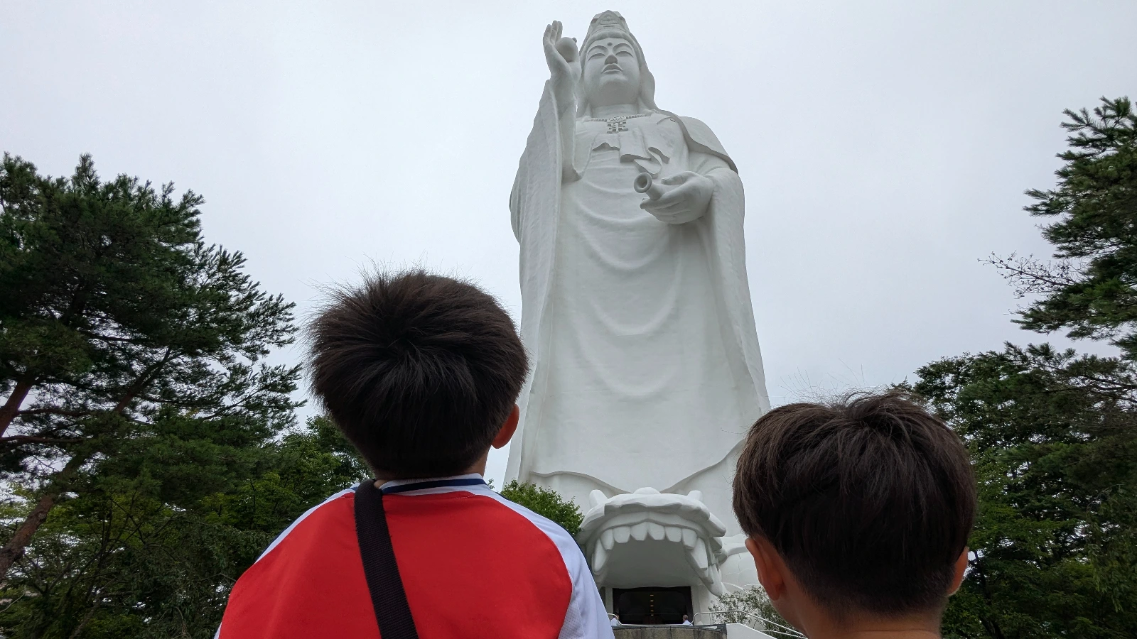 Two children look up at the Sendai Dai Kannon White-Robed Colossus statue, capturing its immense height and sense of wonder for family travelers.