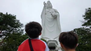 Children looking up at the towering Sendai Dai Kannon statue, one of the tallest statues in the world and a must-see family attraction in Sendai.