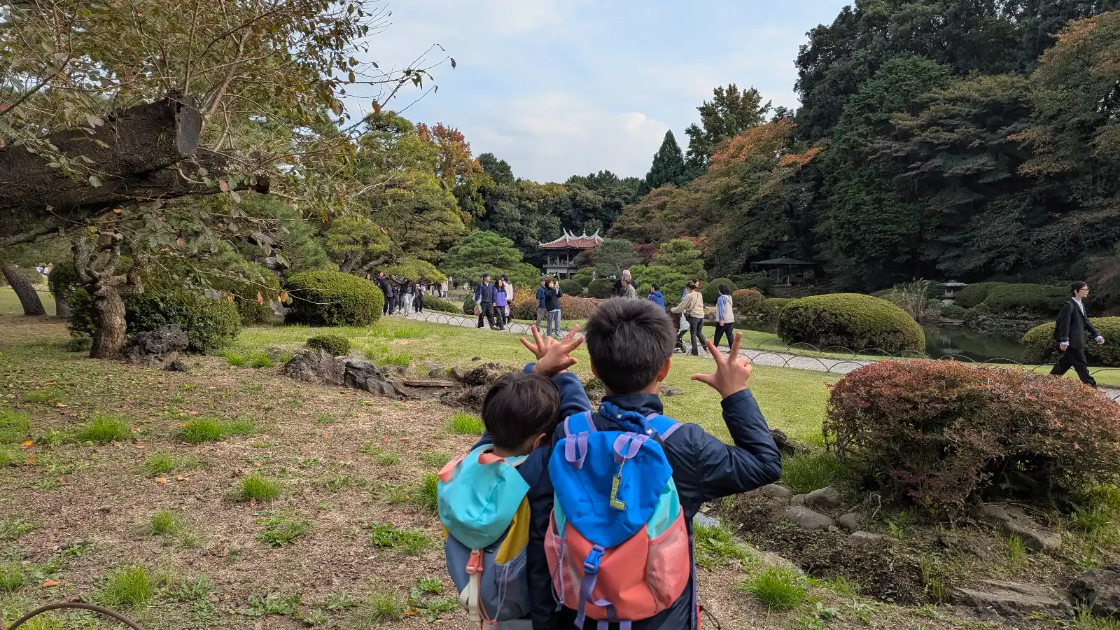 Kids looking across the Japanese Garden at Shinjuku Gyoen National Garden during autumn, with trees, lawns, and a traditional pavilion.