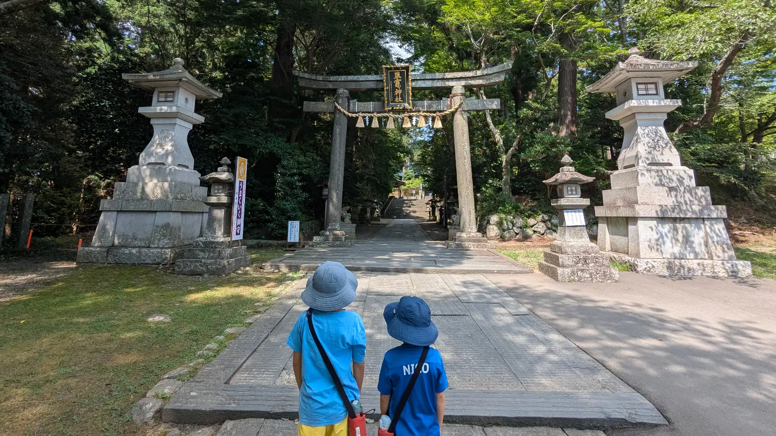 Two children stand before the stone torii entrance of Shiogama Shrine in Sendai, Miyagi — a family travel moment in Japan.