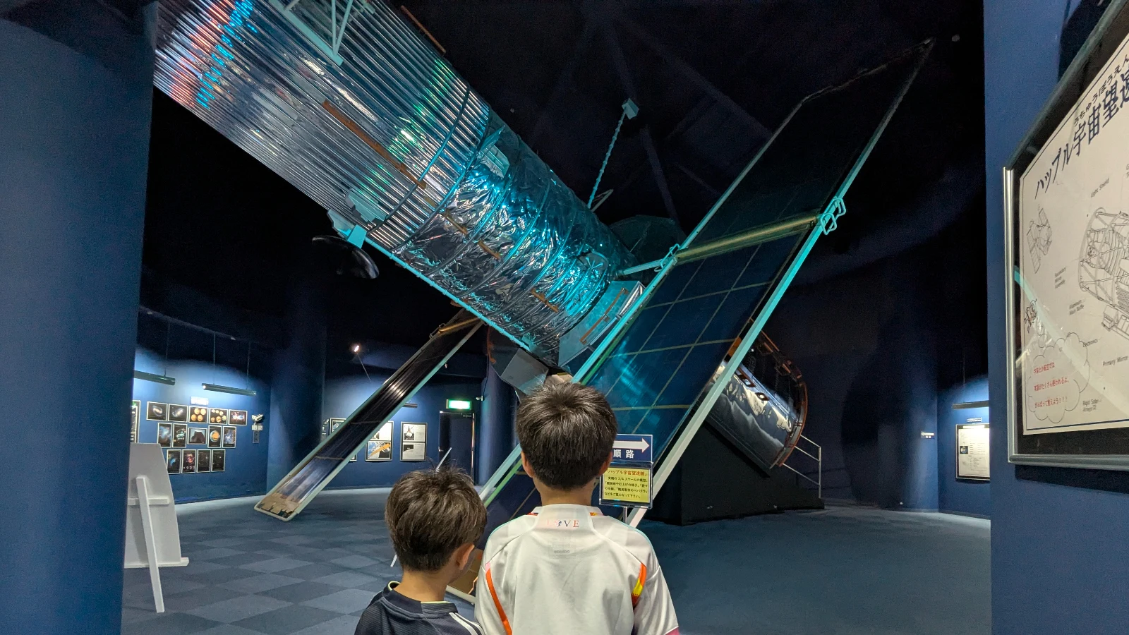 Two children explore a large satellite exhibit inside the Space Dome Yoichi near Otaru, Japan, learning about space and science during a family trip.