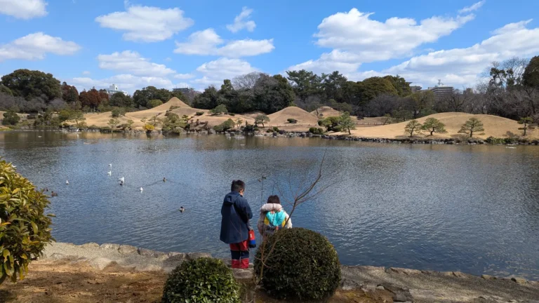 Kids standing by the pond at Suizenji Jojuen Garden in Kumamoto, looking at ducks and the miniature landscape hills across the water.