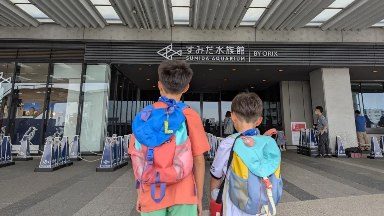 Luca and Nico standing with backpacks in front of the entrance to Sumida Aquarium in Tokyo Skytree Town, ready for a family-friendly aquarium adventure.