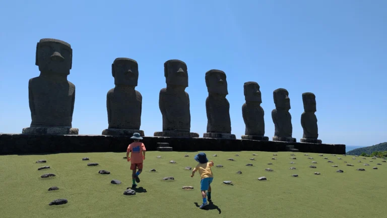 Luca & Nico running toward giant Moai statues under a clear blue sky at Sun Messe Nichinan, one of Miyazaki's top family attractions.
